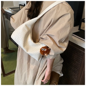 Detail of white woven texture shoulder bag with a cute brown plush monster charm accessory