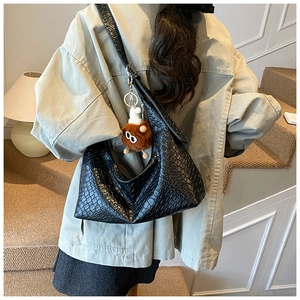 Detail of black crocodile texture shoulder bag with a brown plush monster charm accent