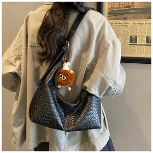 Close-up of woven black hobo bag with a cute brown plush monster charm on the shoulder strap