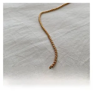 Detail of elegant gold box chain strap on soft white textured fabric background