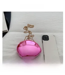 Detail of rose red mirrored oval clutch bag with delicate gold chain strap on white fabric