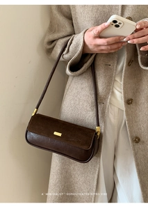 Minimalist shoulder bag detail showing leather texture and gold metal accents on model