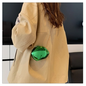 Fashionable bright green metallic mini crossbody bag with a gold chain on a trench coat