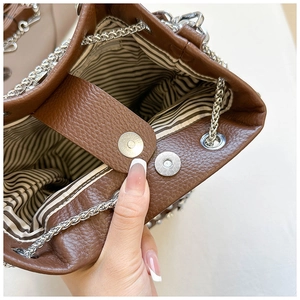 Dettaglio borsa a secchiello in pelle marrone con fodera a righe e chiusura magnetica