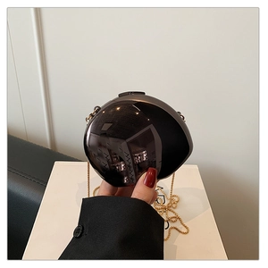 Detailed close-up of glossy black spherical clutch bag with golden chain and mirror finish