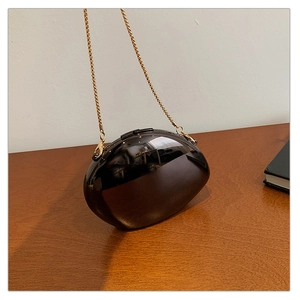 Detail of a sleek black pebble clutch bag featuring a metallic finish and gold chain strap