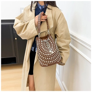 Borsa a secchiello marrone con borchie e catena di perle indossata con trench kaki