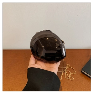 Close-up of gloss black egg-shaped acrylic clutch bag with modern gold chain detail