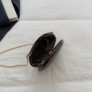 Macro shot of dark brown glossy evening clutch with gold chain and open side view