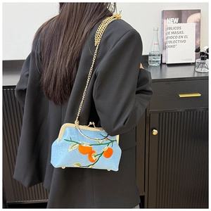 Detail of light blue embroidered kiss-lock bag with orange fruit pattern and gold chain