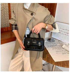 Close-up of black snake pattern handbag with metal buckle detail worn with a trench coat