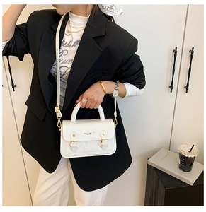 Close-up of a white textured leather crossbody box bag styled on a female model