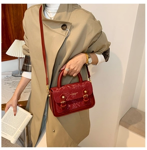 Close-up of burgundy snake print crossbody bag with gold buckle hardware on a coat