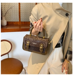 Detail of dark brown handbag with snake pattern texture and gold buckle decorations