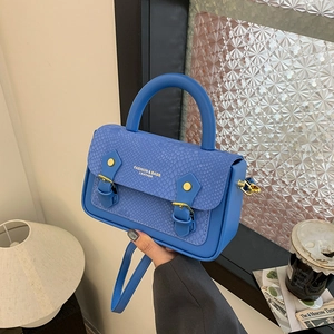 Detail of royal blue handbag featuring snake pattern texture and gold buckle accents