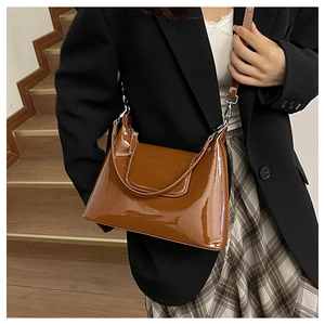 Detail of glossy brown patent leather shoulder bag with metallic silver buckle on a model