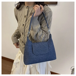 Detail shot of a dark blue denim texture shoulder bag with silver metal hardware accents