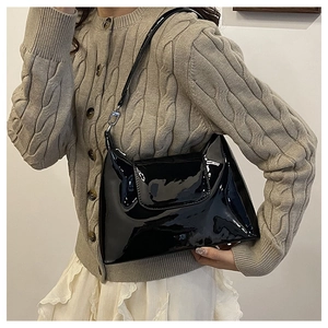 Detail of glossy black patent leather shoulder bag with metallic buckle and slim strap