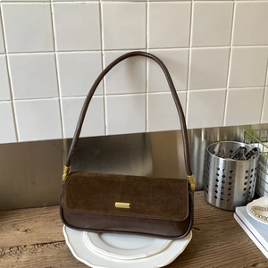 Minimalist brown suede baguette shoulder bag with gold metal trim on wooden table