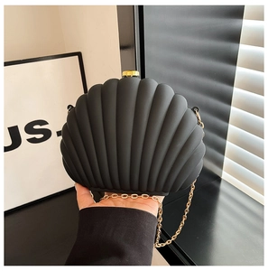 Detail of the black shell-shaped clutch bag with matte texture and gold chain strap