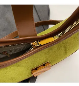 Close-up of smooth gold zipper and contrast leather trim on green suede handbag