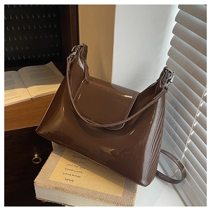 Detailed view of dark brown patent leather shoulder bag on books with silver buckle