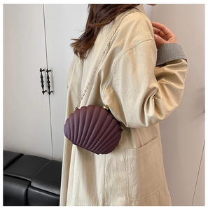 Close-up of wine red shell-shaped evening bag with matte finish and gold chain strap