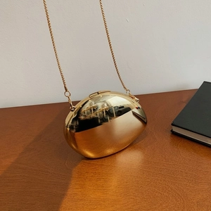 Sleek gold pebble clutch with acrylic chain, minimalist evening bag on wooden surface