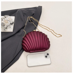 Detailed view of burgundy shell-shaped clutch bag with golden chain and phone for scale