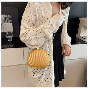 Detail of ginger yellow shell-shaped acrylic bag with gold chain strap on model