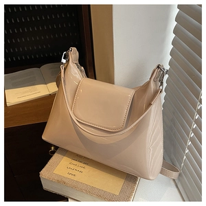 Detail of glossy beige patent leather bag on a wooden table with soft lighting