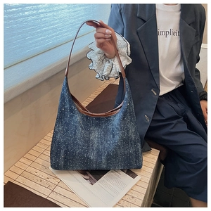 Detail of dark blue denim hobo bag featuring silver rivets and a brown leather strap