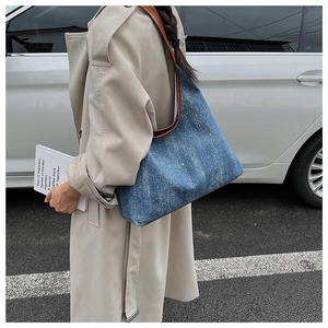 Detail of blue denim tote bag with brown leather straps worn with a beige trench coat