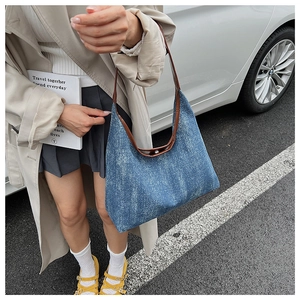 Outdoor shot showing wide opening and brown leather handle of blue denim canvas tote bag