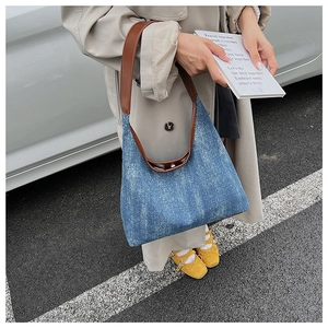 Blue denim tote bag with brown leather straps shown on a model in an outdoor setting