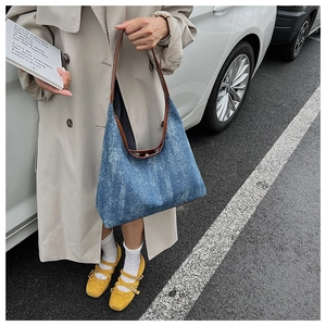 Blue denim tote bag with brown leather straps shown in a street style street look