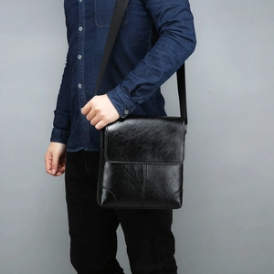Detail of classic black leather messenger bag featuring wide strap and flap closure