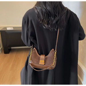 Close-up of brown suede hobo bag with gold chain strap on a model wearing a black coat