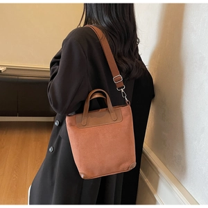 Detail of a brown suede tote bag featuring reinforced leather trim and a wide canvas strap