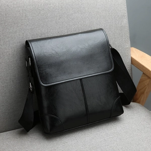 Retro black leather messenger bag with wide nylon strap on a grey fabric chair