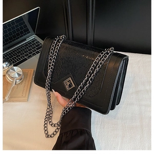 Detail of black crossbody bag with snakeskin texture and silver metal hardware accents