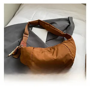 Dettaglio borsa a mezzaluna in nylon caramello con tracolla regolabile e ciondolo di perle