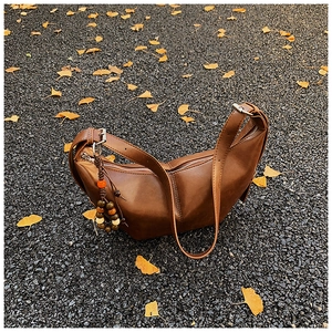 Sac demi-lune marron avec breloque en bois ethnique sur fond de feuilles d'automne