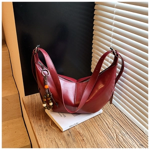 Détail du sac demi-lune en cuir bordeaux avec pompon perlé décoratif sur rebord en bois