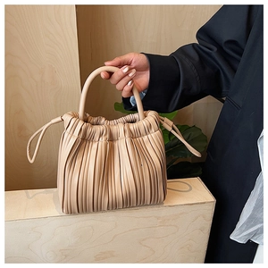 Detail of pleated beige handbag with drawstring closure and curved hard handle on a wood backdrop