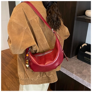 Détail d'un sac cabas demi-lune rouge foncé avec pompon perlé et bandoulière réglable