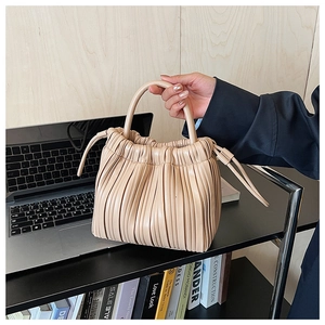 Detail of beige pleated handbag with vertical accordion folds and side drawstring accents