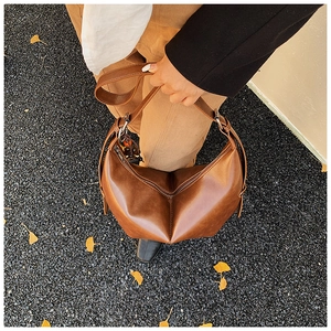 Gros plan du sac hobo en cuir marron avec détail zippé sur fond de feuilles d'automne