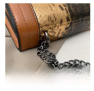 Macro shot of gold snakeskin chain bag showing metal ring and brown leather stitching