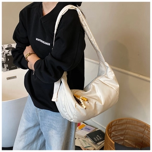 Dettaglio borsa a mezzaluna in nylon crema con ciondolo di perline colorate sul modello